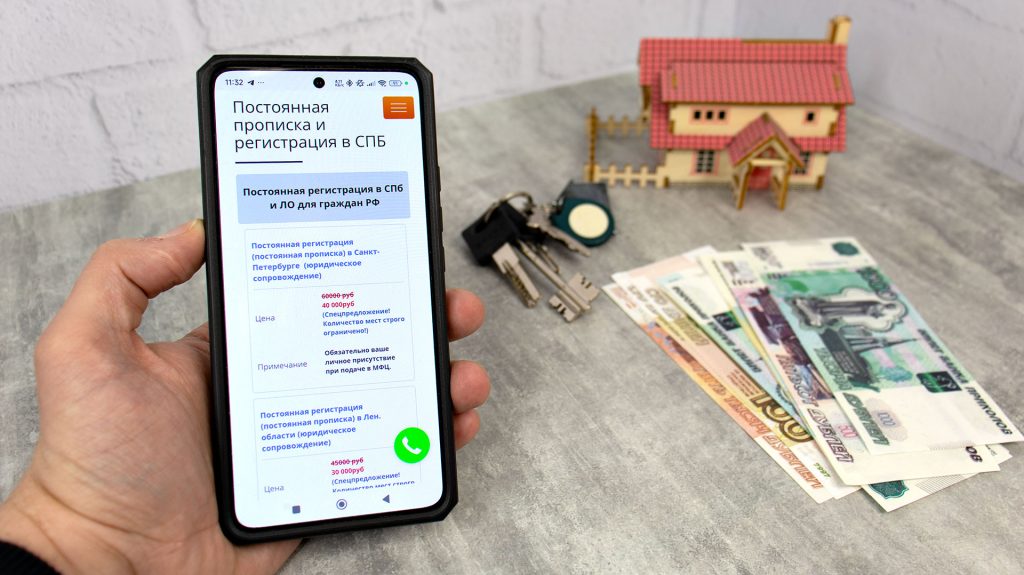 Смартфон с объявлением о платной прописке и деньги на столе рядом с ключами и макетом дома
