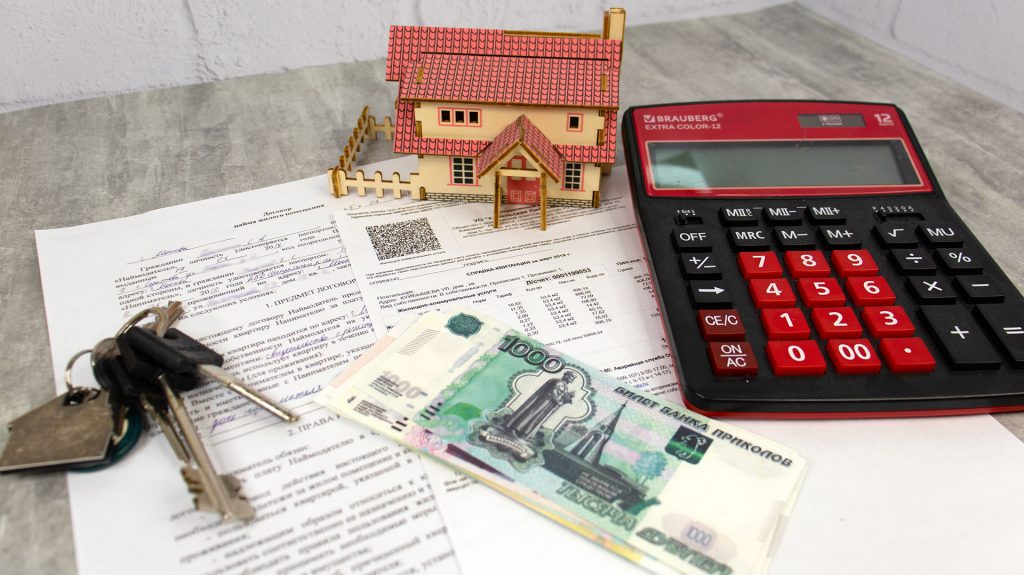 Калькулятор, ключи, платежные документы и деньги на столе рядом с макетом дома