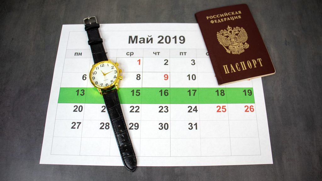 Календарь, наручные часы и паспорт гражданина РФ на фоне.